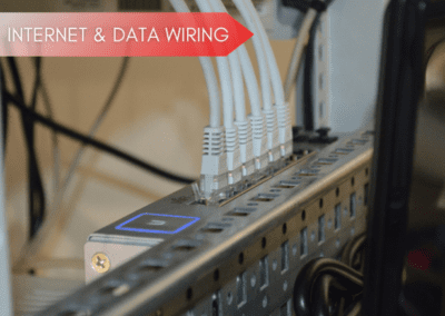 Close-up of several Ethernet cables plugged into a network switch, with a label in the top left corner reading "Internet & Data Wiring.